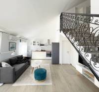 Living area in a holiday apartment with a kitchen, sofa, and staircase.