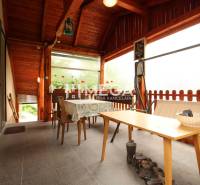 A veranda in a family house with a wooden ceiling, table, chairs, and flowers.