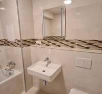 Bathroom in a studio apartment with a bathtub, sink, and toilet, tiles with a decorative strip.