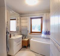 A bathroom in a family house with a bathtub, a window, and a sink with storage space.