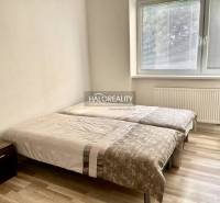 A bedroom in a three-room apartment with two beds, a nightstand, and a large window.