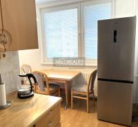 A kitchen in a 3-room apartment with a refrigerator, a wooden table, and chairs.