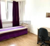 Room: bed with a purple blanket, desk, black chair, window with purple curtains.