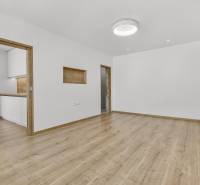 Spacious living room with wooden flooring and entrance to the kitchen in a 4-room apartment.