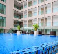 A swimming pool under construction in a residential complex in Pattaya, surrounded by glass buildings and lounge chairs.