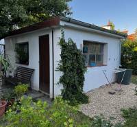 A family house in Lučenec with a garden house surrounded by greenery and a bench.