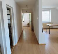 A hallway with a wooden floor, rooms on the left, a room with a table on the right in a family house.