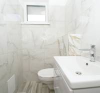 A bathroom with a sink, ceramic tiles, and a toilet in a family house.