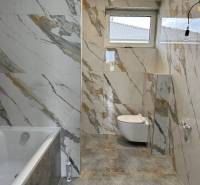 A bathroom in a family house tiled with a marble pattern, featuring a bathtub and a toilet.