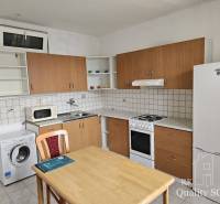 Kitchen area of a 2-room apartment with a refrigerator, washing machine, and stove, wooden table with a chair.