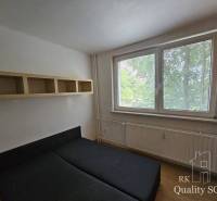 A bedroom in a 2-room apartment with a bed, a shelf, and a window with a view of greenery.