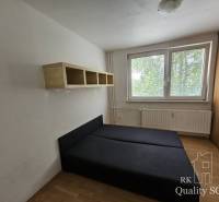 A bedroom with a bed and a shelf in a two-room apartment. Windows with a view of greenery.