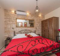 A bedroom in a family house with a stone wall, a metal bed, and a wooden wardrobe.