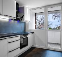 A kitchen in a 3-room apartment with white cabinets, a black cooking surface, and a window.
