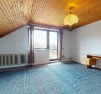 A room with a wooden ceiling, a writing desk, and a large window in a family house.