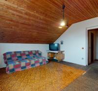 Attic room with a wooden ceiling, a couch, and a television in a family house.