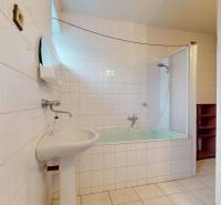 A bathroom in a family house with white tiles, a sink, and a bathtub with a shower.