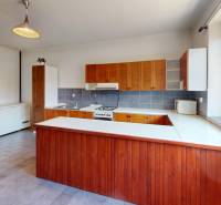 A kitchen in a family house with wooden cabinets, appliances, and a large window with a view.
