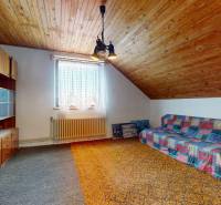 An attic room in a family house with wooden ceiling paneling, a sofa, and shelves.