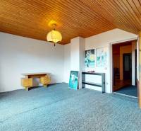A room in a family house with a sloped ceiling, carpet, and simple furniture.