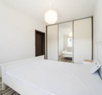 A bedroom in a two-room apartment with a white bed, a mirrored wardrobe, and a light interior.