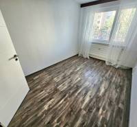 An empty room with laminate flooring and a large window in a three-room apartment.
