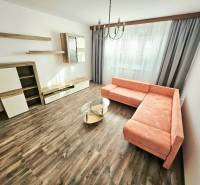 Living room of a three-room apartment with a corner sofa, curtains, and wooden floor.