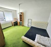 A room in a 3-room apartment with a bed, a table, and a green carpet.