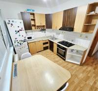 A kitchen in a 3-room apartment with a stove, refrigerator, and wooden table.