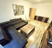 Living room in a three-room apartment with a black sofa and wooden furniture.