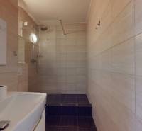 A bathroom in a 4-room apartment with a sink, shower, and light tiles.