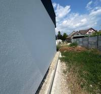 The wall of a family house in Žihárec with an adjacent plot of land under the blue sky.