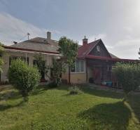A family house in Hrkovce with a garden, shrubs, and a wooden shelter.
