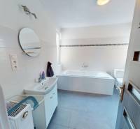 A bathroom in a family house with a bathtub, mirror, and sink, light tiles.