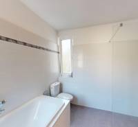 A bathroom in a family house with a bathtub, shower, and toilet, tiled with light tiles.