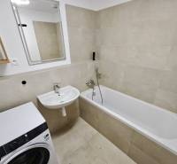 Bathroom in a 3-room apartment with a bathtub, sink, and washing machine, beige tiles.