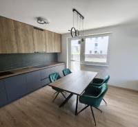 A kitchen in a 3-room apartment with wooden and dark cabinets, a dining table, and emerald chairs.