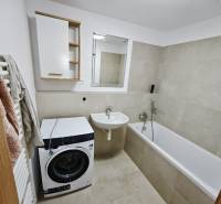 Bathroom in a 3-room apartment with a washing machine, bathtub, and sink in light shades.