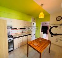A kitchen with green walls, white cabinets, and a dining table in a three-room apartment.