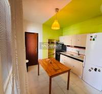 A kitchen in a 3-room apartment with a green wall, a wooden table, and white cabinets.