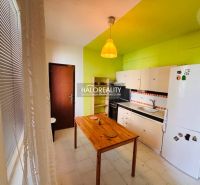 A kitchen in a 3-room apartment with a green wall, a wooden table, and white cabinets.