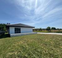 A family house in Podlužany with a large lawn, next to a dirt road and a fence.