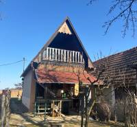 A cottage with a sloped roof and a veranda, surrounded by garden recreational grounds.