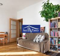 Studio apartment with wooden flooring, a sofa, a bookshelf, and a dining table.