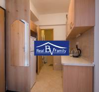 Kitchen corner in a studio apartment with a wooden kitchen unit and ceramic floors.