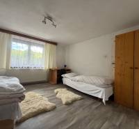 A room with two beds, a wooden wardrobe, a table, and carpets in a family house.