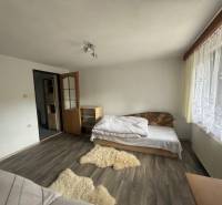 A room with a bed, wooden floor, and a window with a white curtain in a family house.