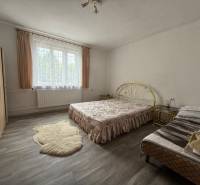 A bedroom in a family house with a bed and a wardrobe, light curtains on the window.