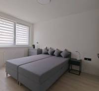 Bedroom in a studio apartment with a double bed, nightstands, and a window with blinds.