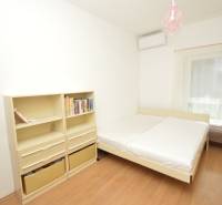 Bright bedroom in a 2-room apartment with a bed, bookshelf, and air conditioning.